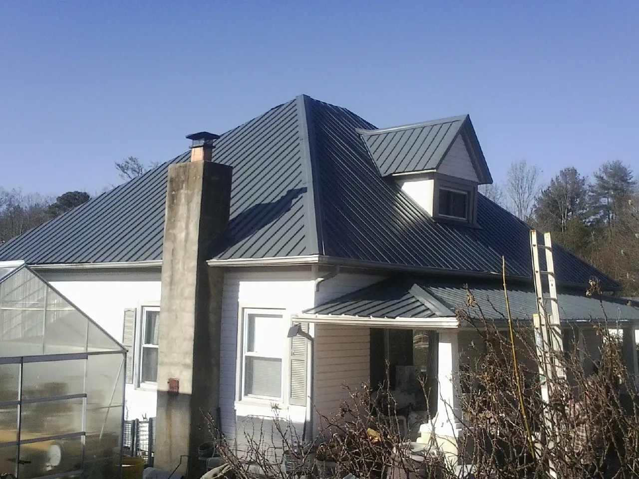 Dark blue standing seam metal roof on a white farmhouse with dormer — Slate & Tile Roof Repair by Roofing Brothers in Holtsville