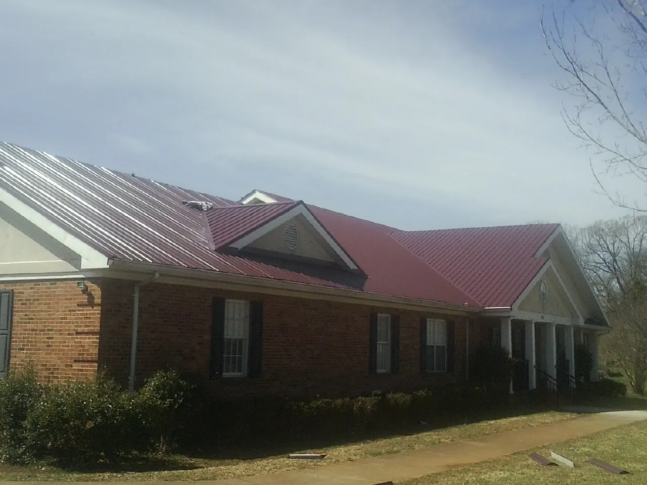 Red metal roof with gabled entries on a long brick building, from a Hail Damage Roof Repair job in Holtsville