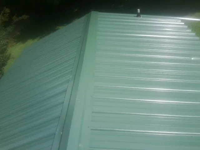 New green metal panels meeting at the ridge of a roof — Flat Roof Repair work by our crew in Holtsville