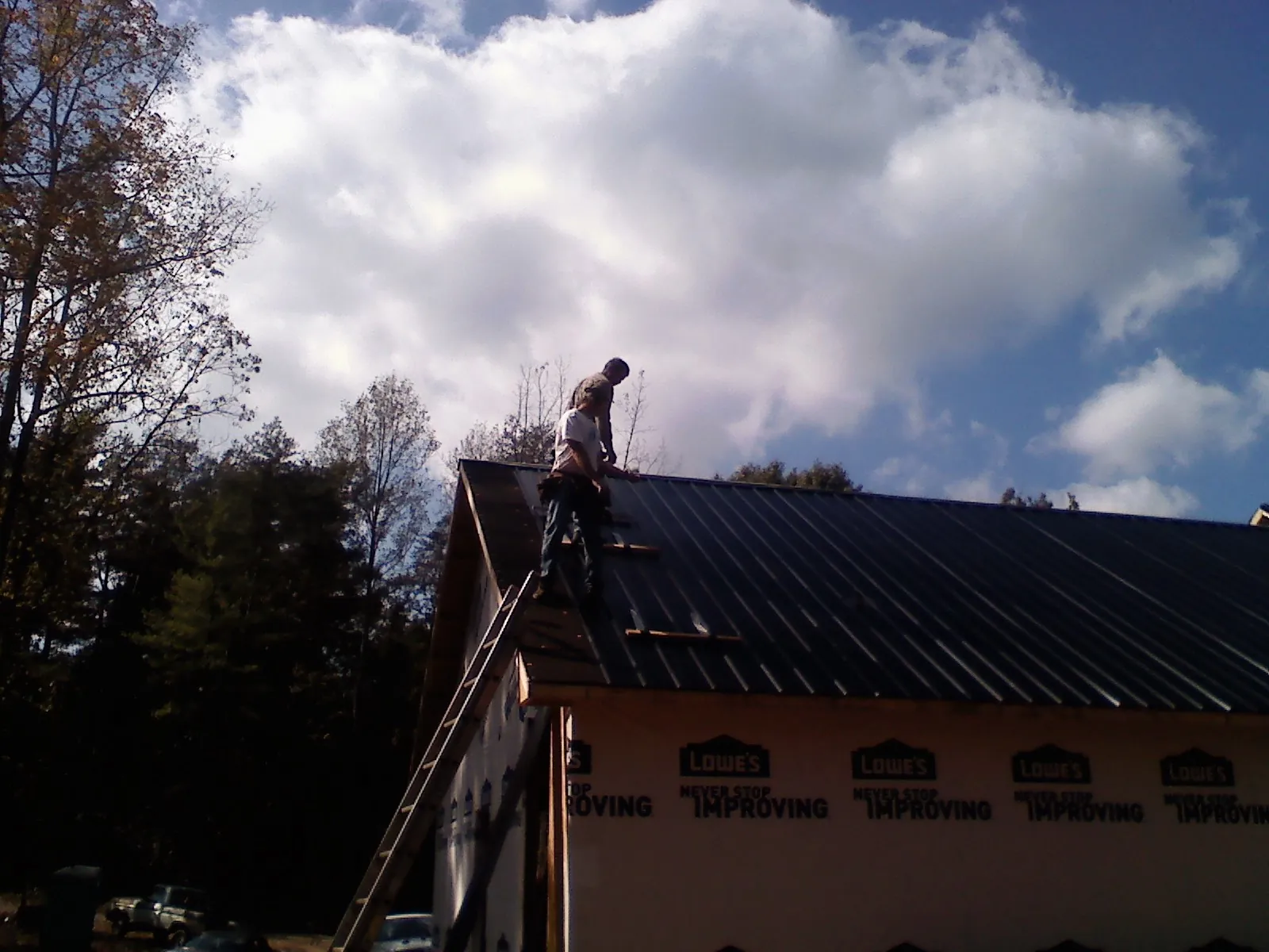 Roofer fastening dark metal panels high against a cloudy sky, from a Roof Inspection job in Holtsville