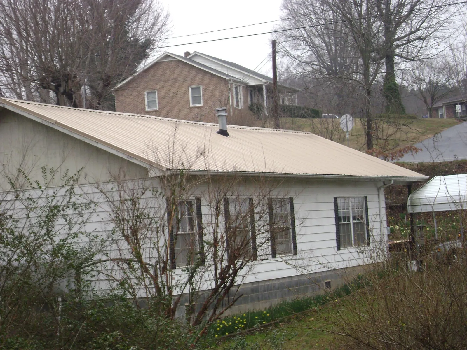 Tan metal roof on a white sided house set into a hillside — Commercial Roofing by Roofing Brothers in Holtsville