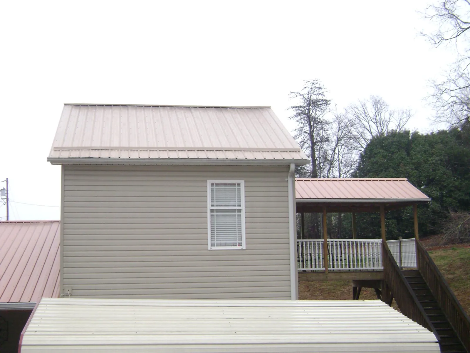 Tan metal roofs on a two story addition and attached porch, from a Roof Replacement job in Holtsville