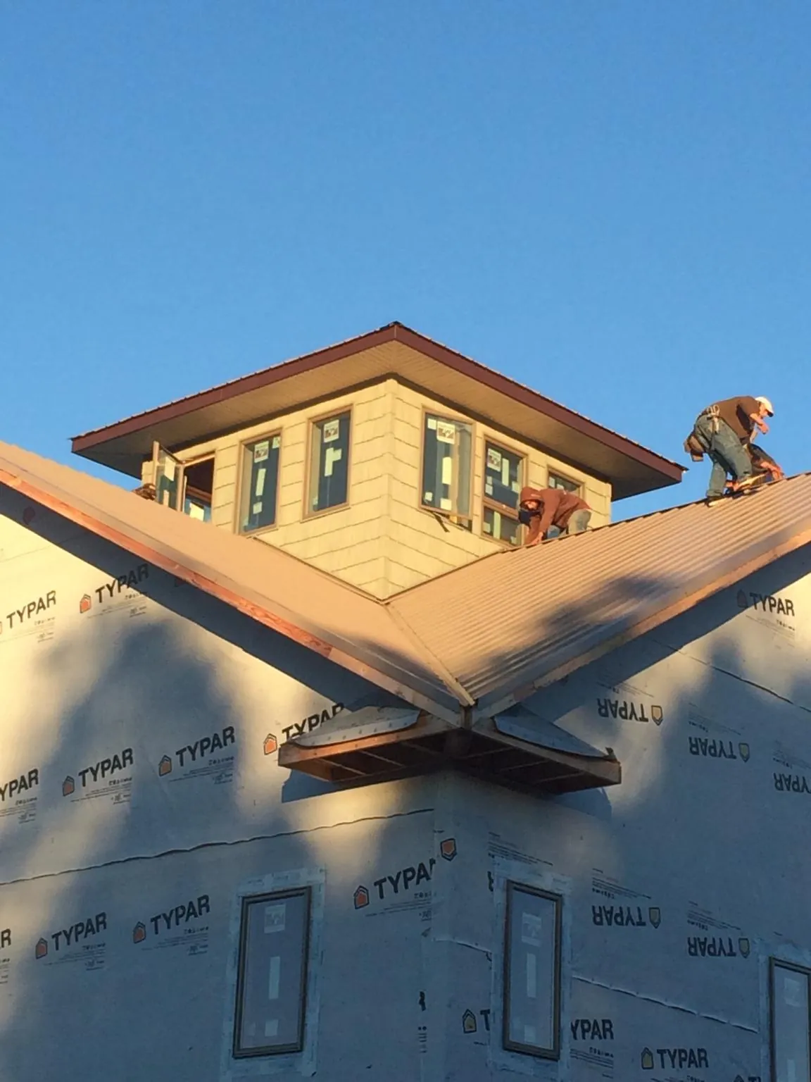 Roofers working around a rooftop cupola on a new metal roof at sunset — Roof Waterproofing in Holtsville by Roofing Brothers